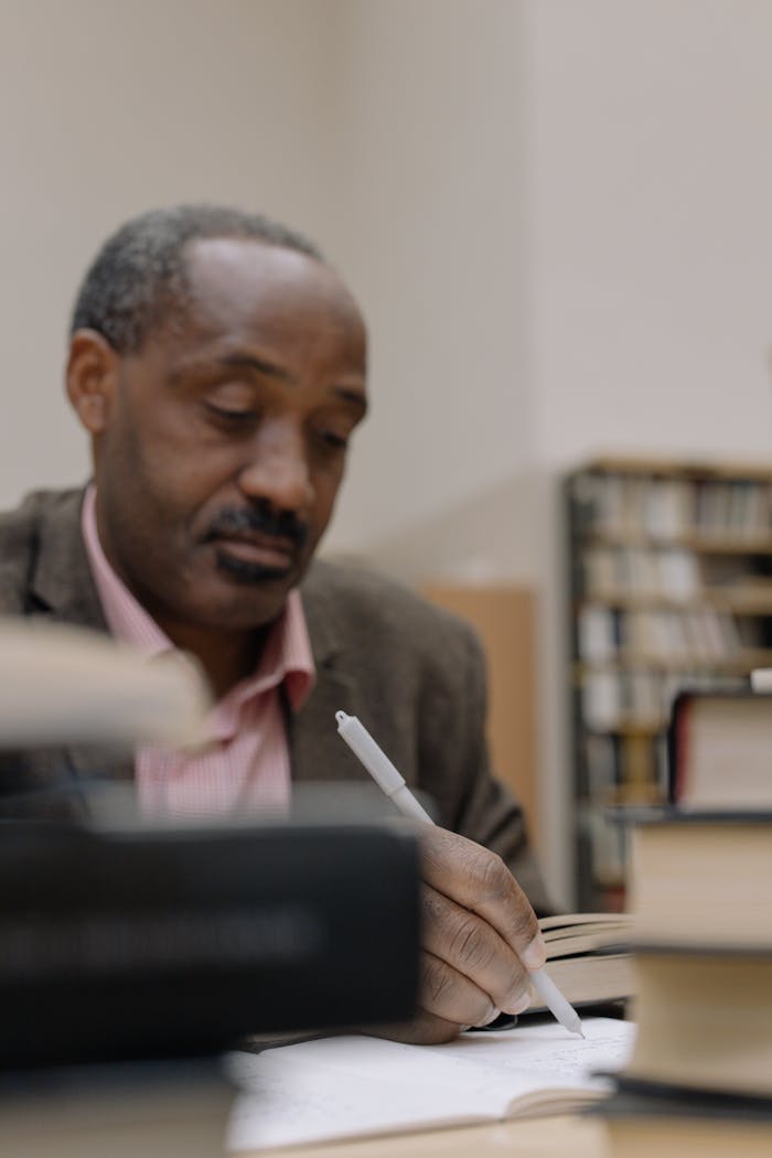 Man deeply focused on studying in a library with books and pen.