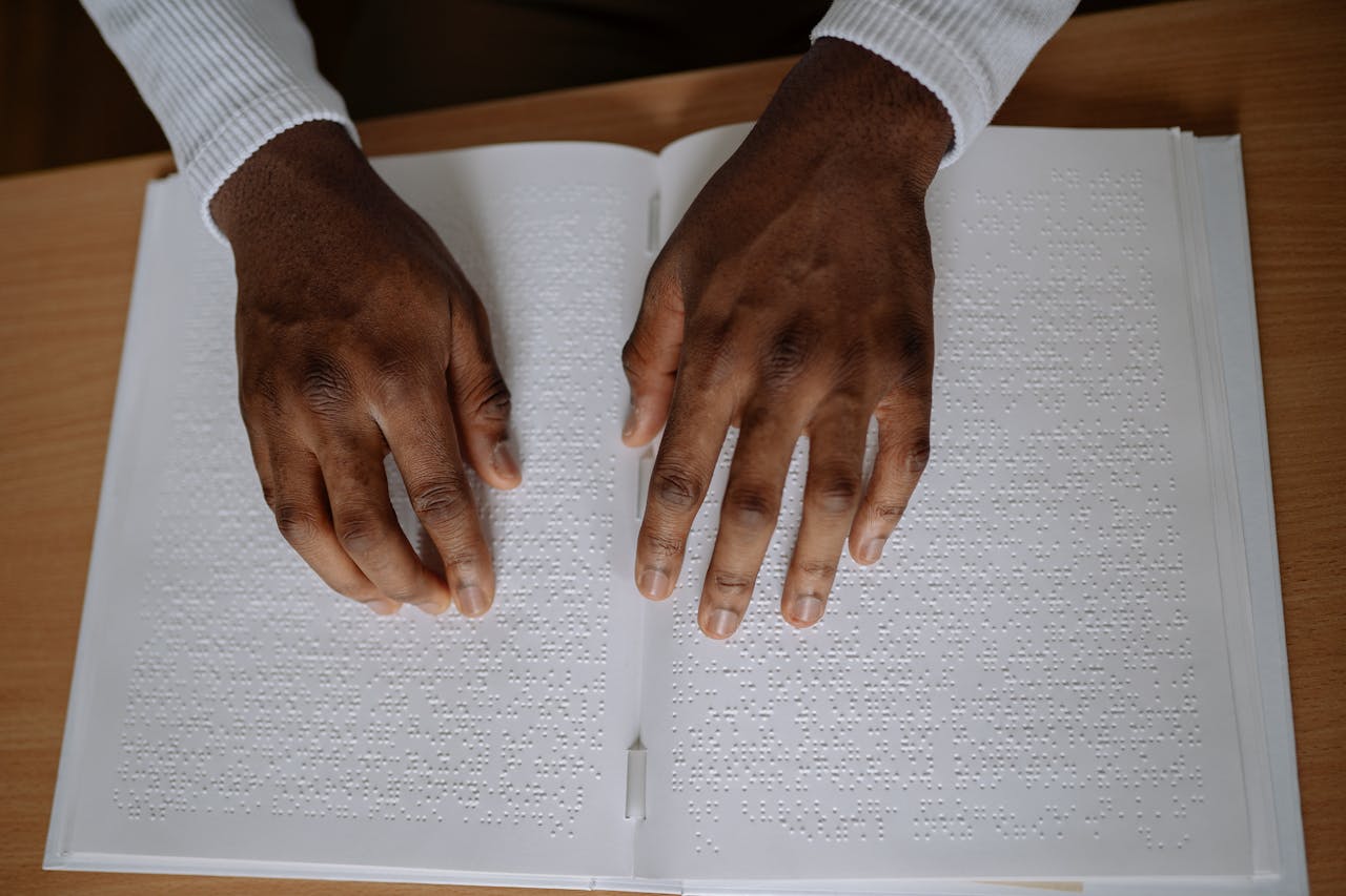 A pair of hands reading a braille book on a wooden table, emphasizing touch and sensory experience.